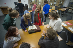 Students in a classroom talking while looking at a book