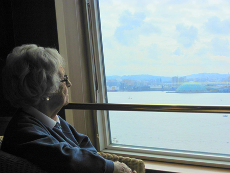 تظهر امرأة مسنة ذات شعر أبيض ونظارات تنظر من النافذة عبر جسم مائي.