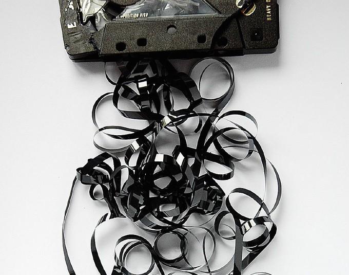A broken audio cassette tape sits on a table with tape spilling out into a messy pile.