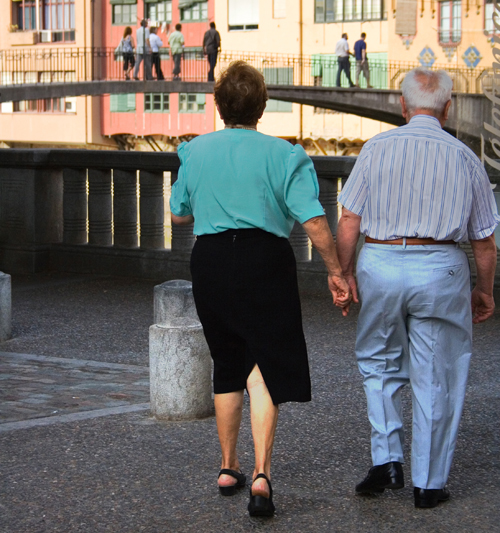 Sur la figure (a), un homme et une femme âgés, vêtus d'une tenue décontractée, sont représentés de dos marchant sur une place publique.