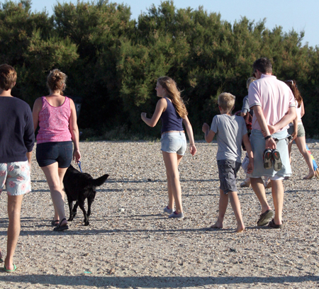 La photo (a) montre une famille marchant avec un chien sur une plage. Photo