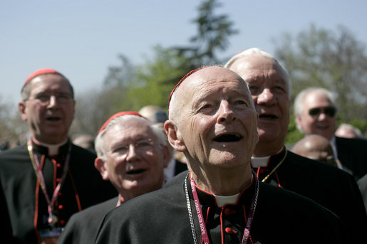 Cerca de meia dúzia de homens mais velhos vestindo trajes sacerdotais católicos romanos são mostrados dos ombros para cima.