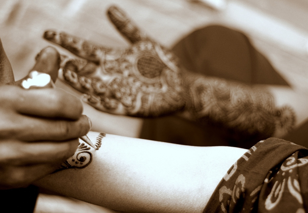 A foto mostra as mãos de uma mulher cobertas por desenhos intrincados de henna.