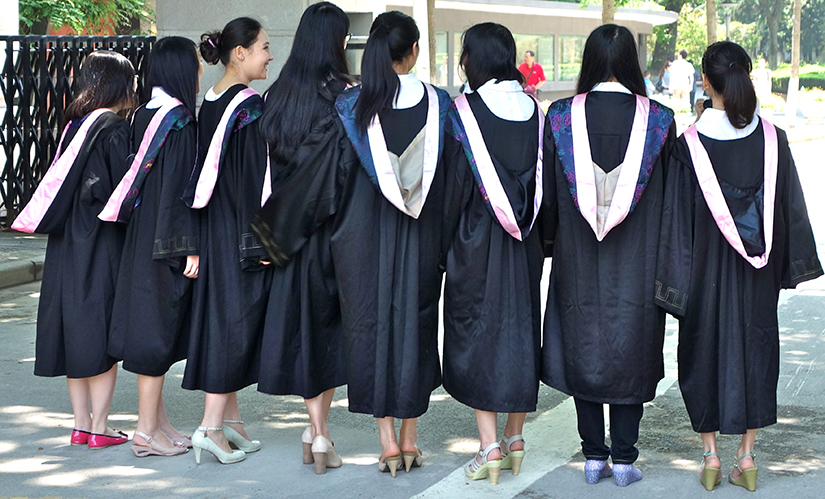 Oito meninas se formando na faculdade em seus vestidos, com as costas voltadas para a câmera