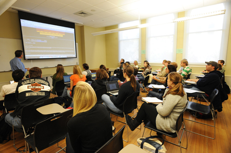 Professor e alunos do ensino médio em uma sala de aula olhando para a tela de projeção na frente da sala de aula.