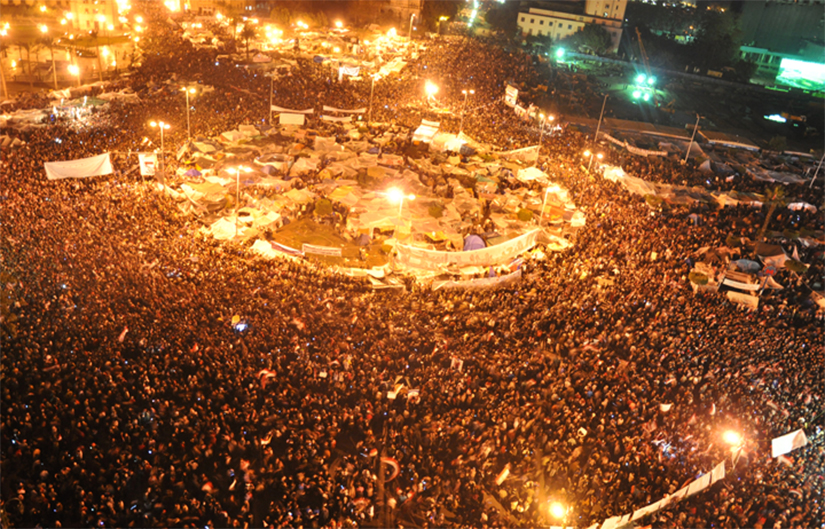 Foto de uma praça Tahirir lotada no Cairo, Egito, onde muitas pessoas na multidão estão levantando bandeiras egípcias no ar