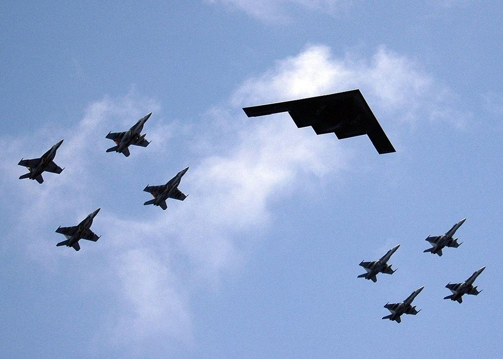 Uma formação de aviões com caças e um bombardeiro furtivo é mostrada no céu.