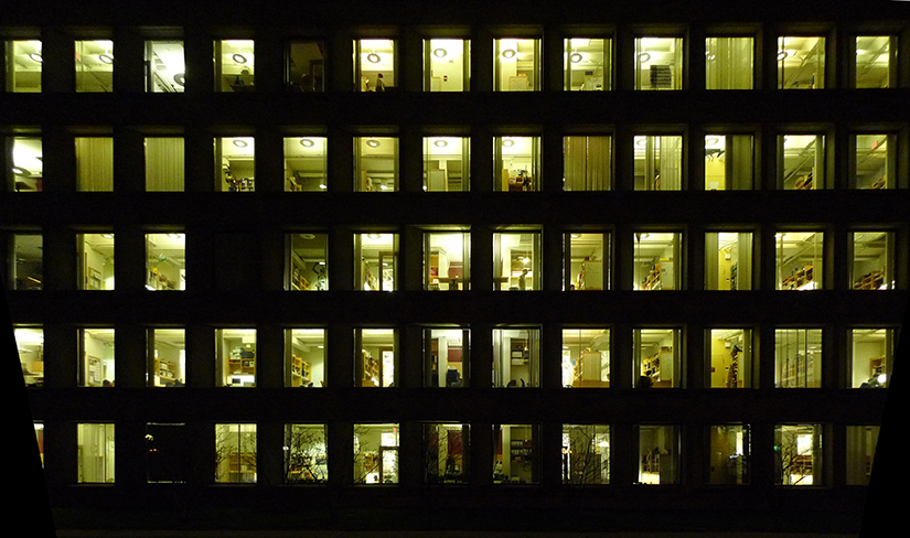 Uma foto de um grande prédio de escritórios à noite, onde você pode ver muitas pessoas trabalhando dentro de casa após o expediente
