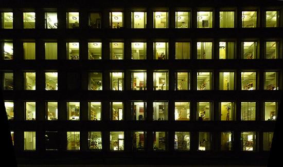  A photo of a large office building at night where you can see many people working inside after hours
