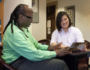A male college counselor meets with a female student, who looks at a resource pamphlet.