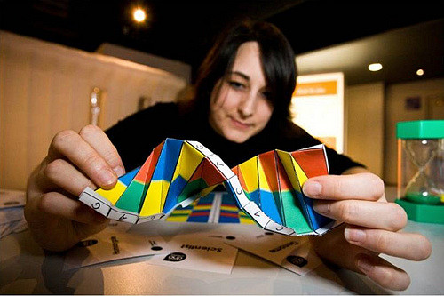 Photo of a young woman holding brightly colored, twisted paper up to the camera, "DNA Oragami"