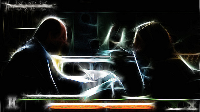 Image of two figures sitting at a table, suggested by light outlines against a black backdrop