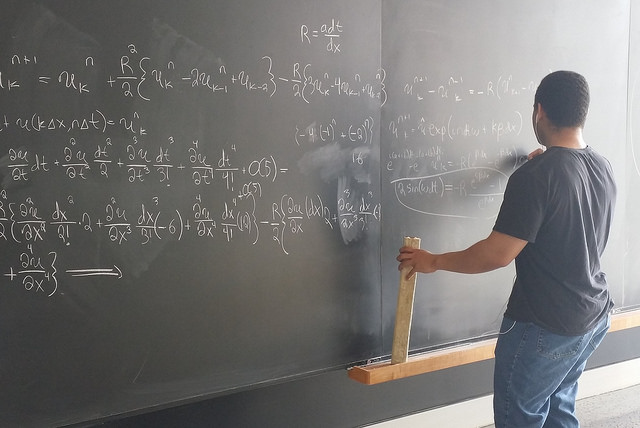 Student working complex math problem on chalkboard