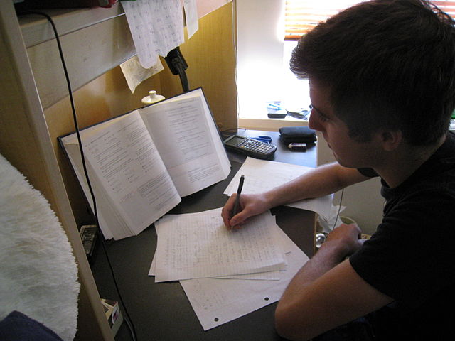 A student taking notes based on his textbook as he reads in the library