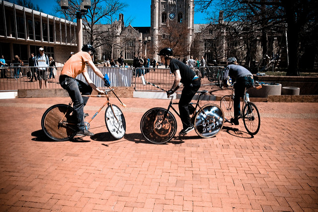 Three young men playing "bike polo" on a brick-paved campus courtyard