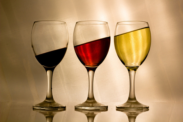 Three wine glasses on a flat surface with dark red, light red, and yellow liquid. The surface level of each liquid is at a tilt that would be impossible on an actual flat surface.