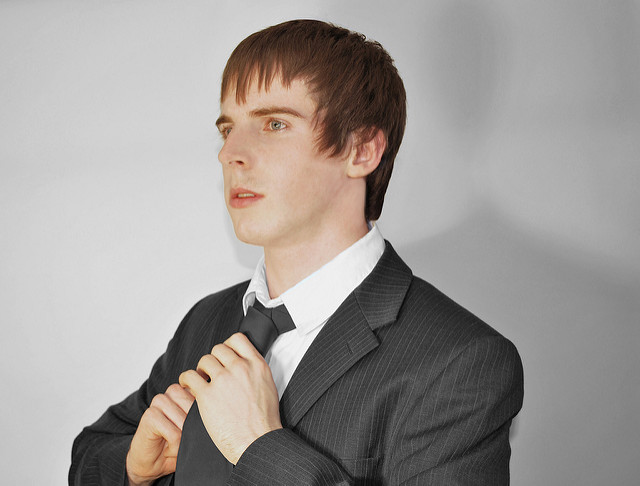Young man around age 20, adjusting his tie for an interview.