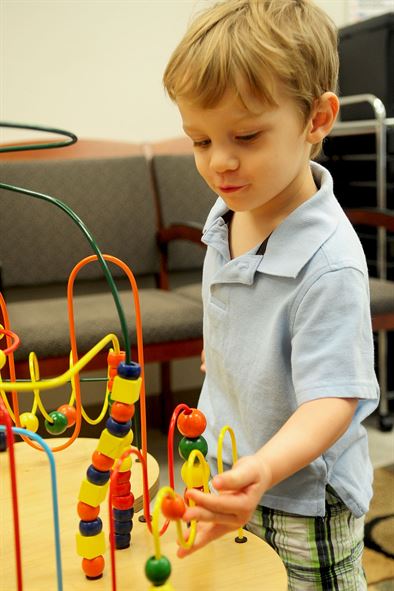 Two year old boy playing with a bead-maze track game in an office waiting room.