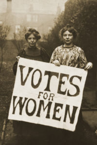 Black and white photograph of two female suffragettes holding a poster saying "Votes for Women"