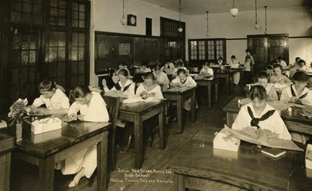 Early 20th century black and white photo of a classroom with female students at their desks.