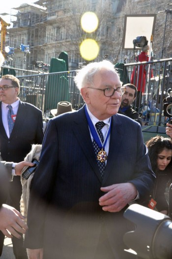 Warren Buffett standing outside among people and photographers.