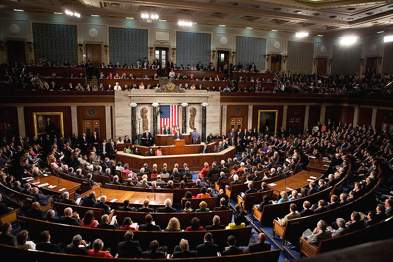 This photo shows rows and rows of people sitting on benches all facing a central point in the room where former president Barack Obama is standing at a pulpit giving a speech.