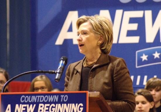 Then-presidential candidate Hillary Clinton is shown speaking into a mic and standing behind a podium with a placard stating: Countdown to a New Beginning.