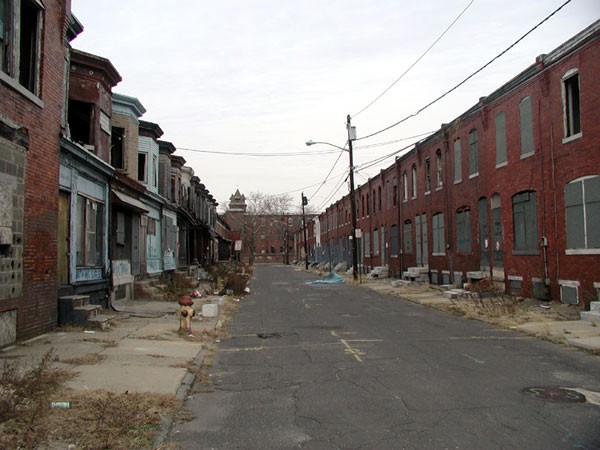 A block of run-down, dirty rowhouses lining an abandoned street are shown.
