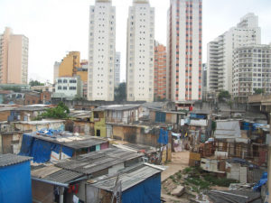 Rundown shacks in the forefront of a picture with large skyscrapers in the distance.