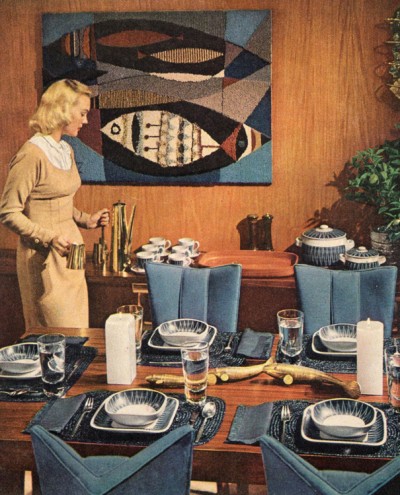 Woman in 1950s or 1960s dress placing coffee on buffet table in a formally set dining room.