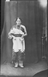 Black and white photo of a Native American Zuni man dressed in tribal attire that would typically be worn by a female..