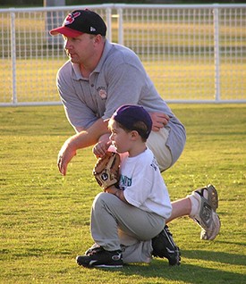This image is of a kneeling man with a small child holding a mitt who is learning to play baseball.