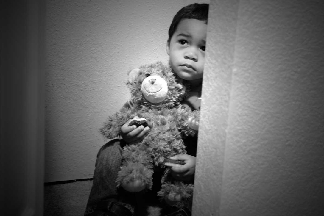 Little boy holding a stuffed animal hiding in the shadows.