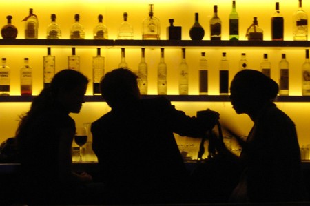 Photo of 3 silhouetted figures drinking at a bar.