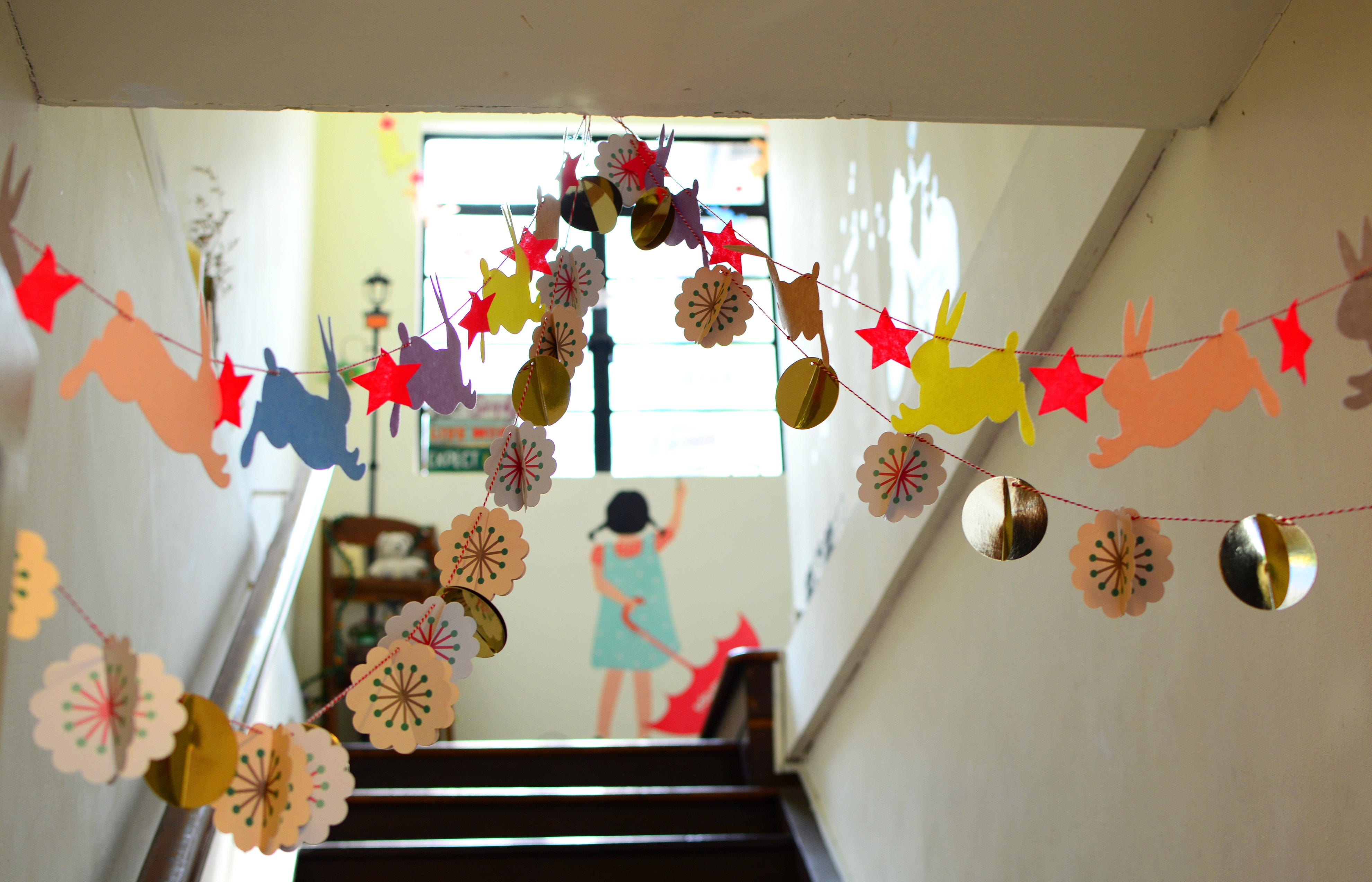There are garlands of paper rabbits and paper flowers hanging from the ceiling of a staircase.