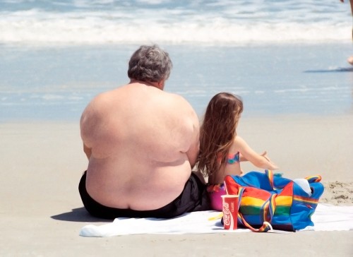 A large man is shown here sitting on a beach next to a young girl.