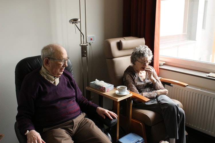 An old man and woman are sitting in chairs next to one another.
