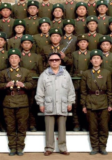 Kim Jong-Il of North Korea is shown wearing sunglasses, standing among a group of uniformed North Korean soldiers.