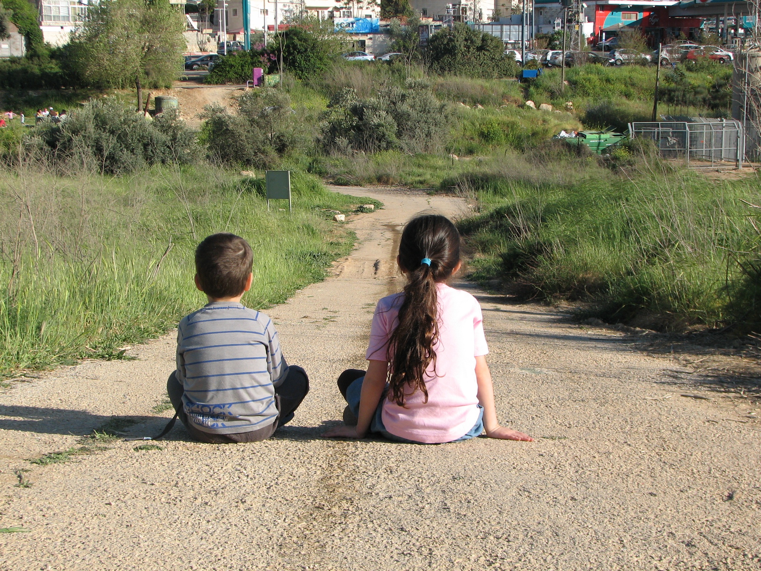 Two children shown from behind sitting on a pathway overlooking a town