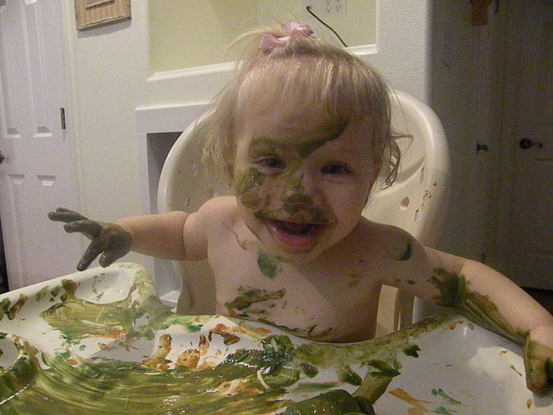 messy toddler girl covered with fingerpaint.