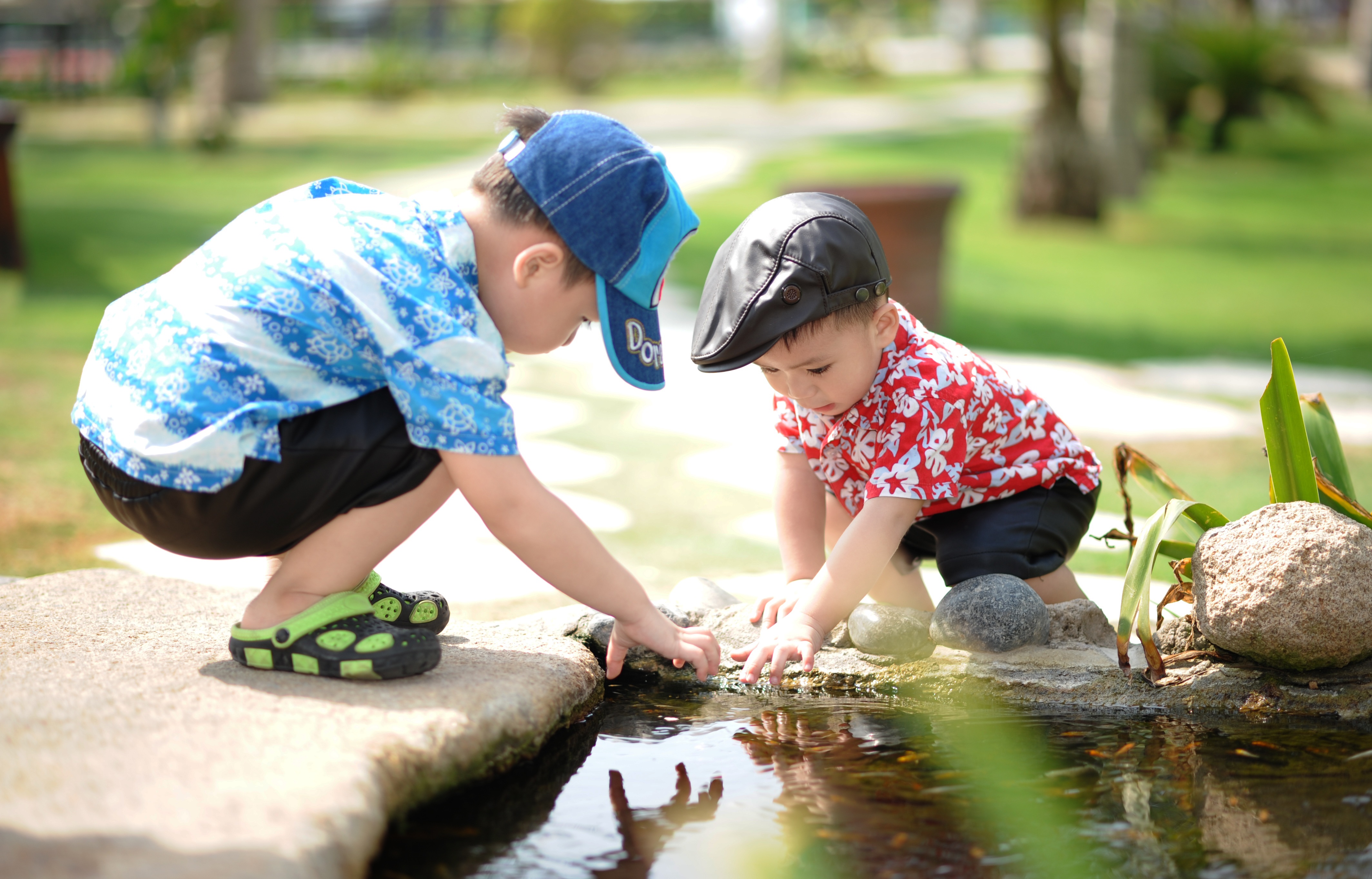 Two boys squatting and playing by a pond