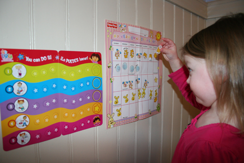 A child placing stickers on a chart hanging on the wall.