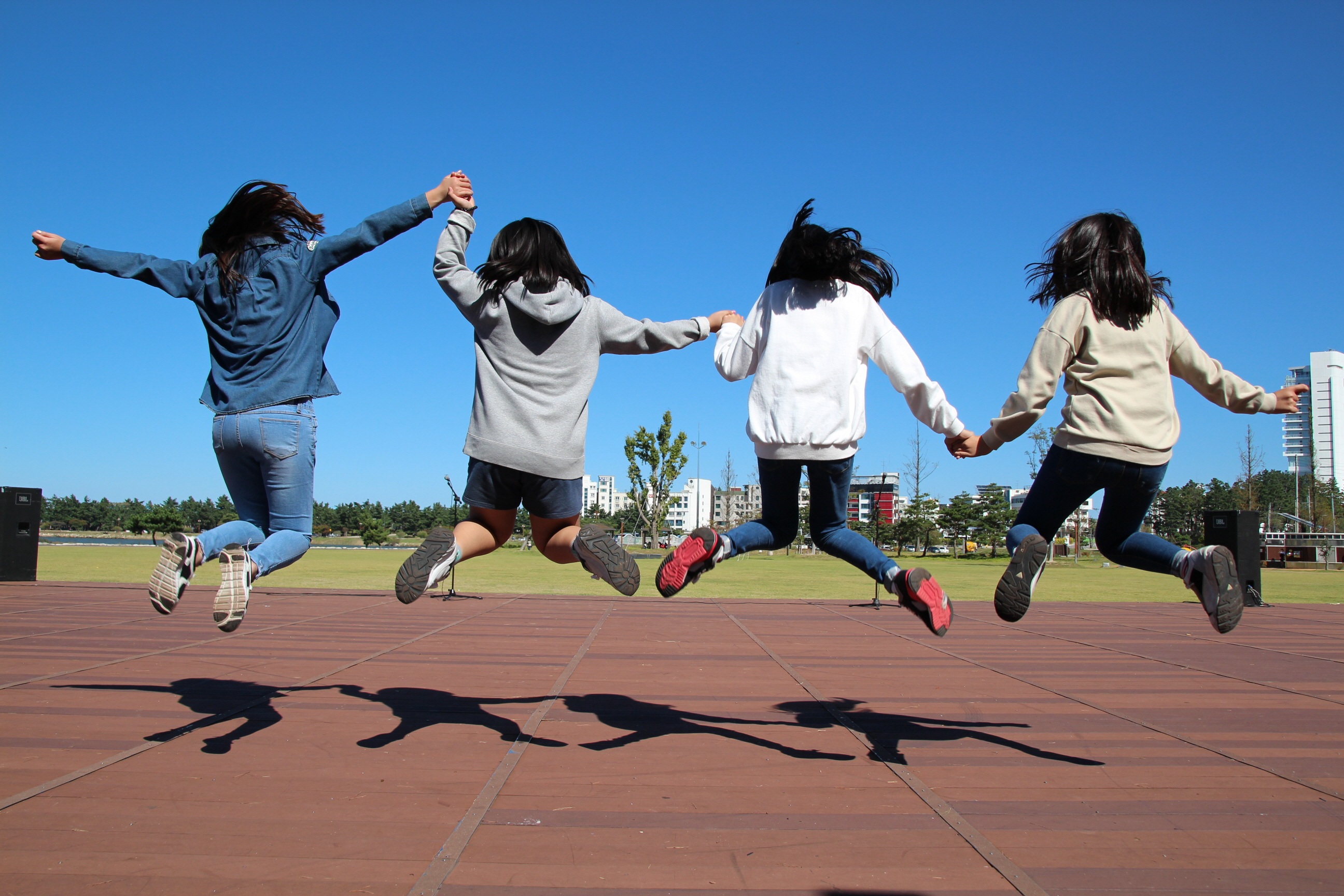 Four girls shown from behind jumping and holding hands
