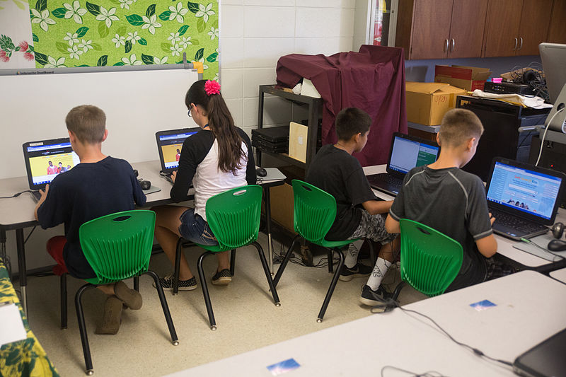 four elementary students sit in front of computers taking a standardized test.