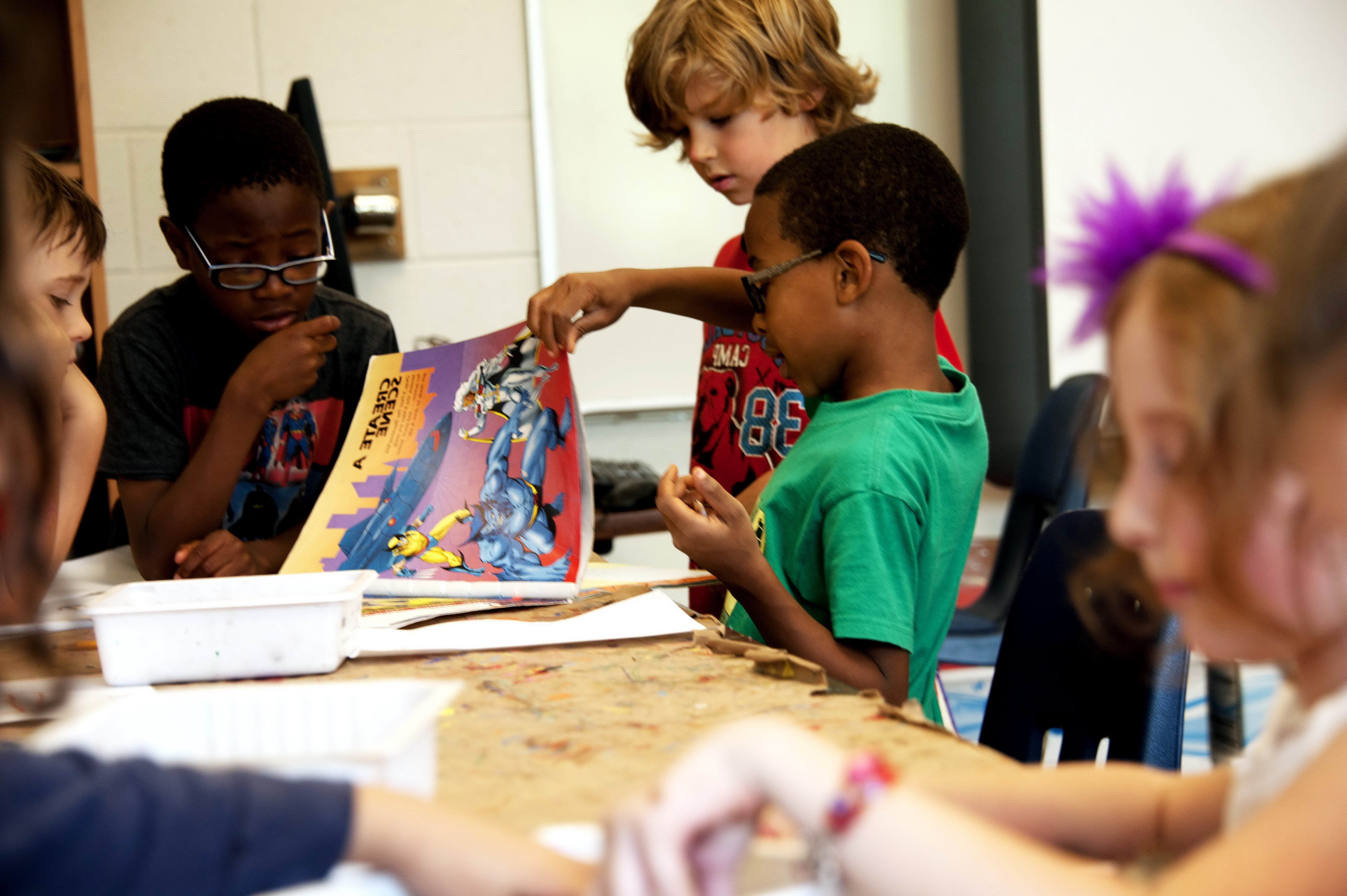 Elementary students talking at a table and sharing a comic book.