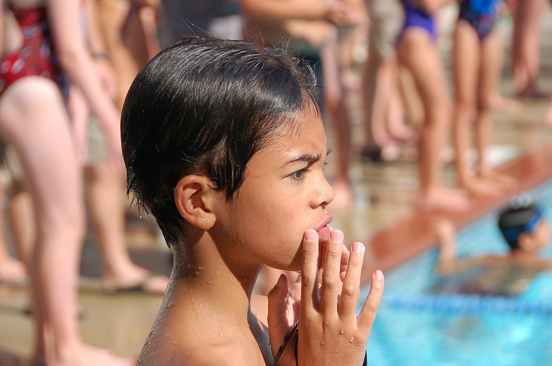 Boy at a swimming pool with a look of reflection on his face.