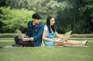 2 people sitting together on the grass looking at their laptops