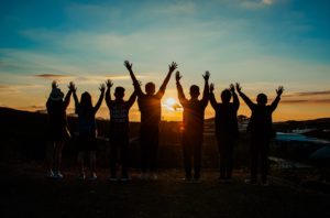 A group of people facing the sunrise with their arms in the air