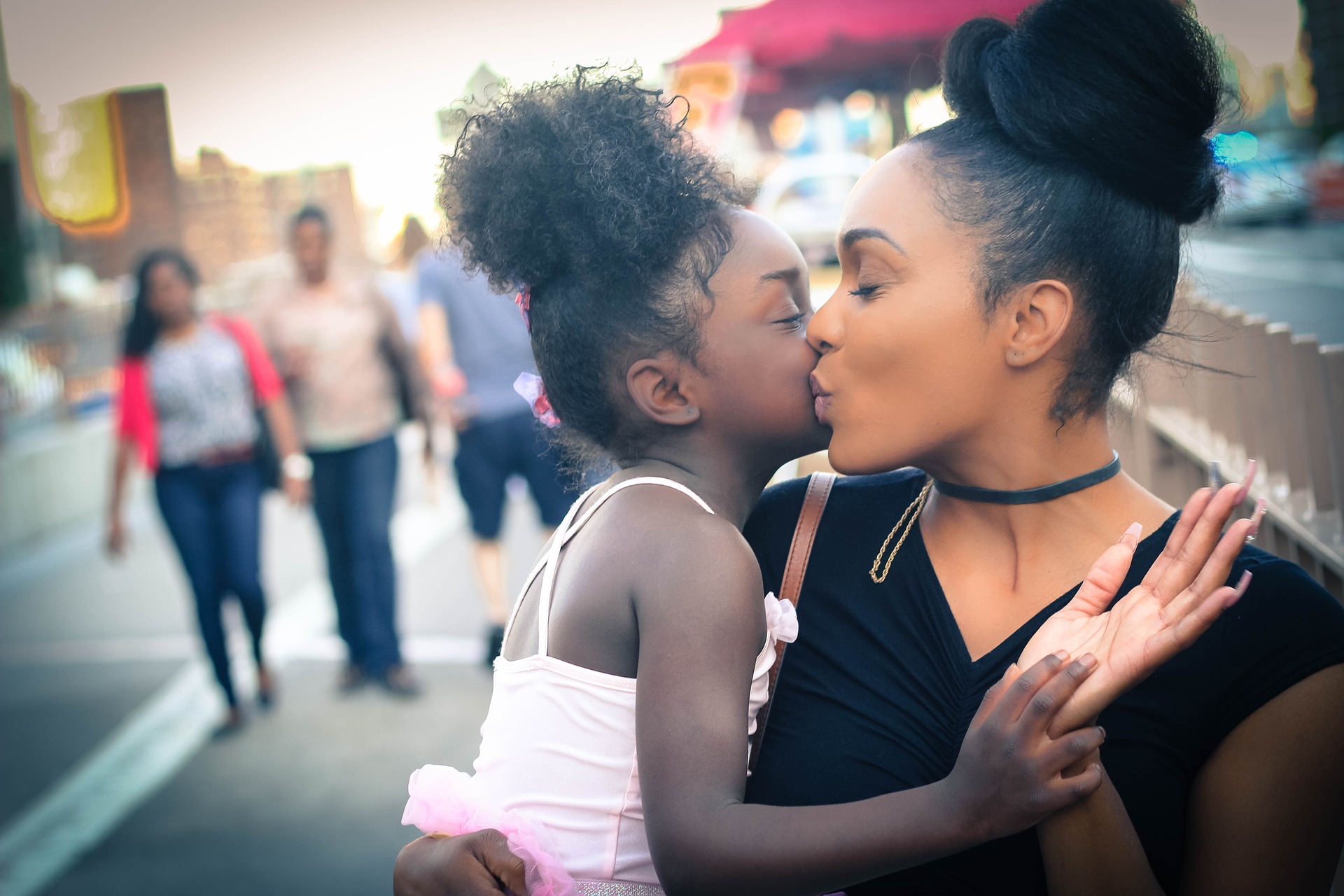A young woman holding a young girl and kissing her on the cheek.