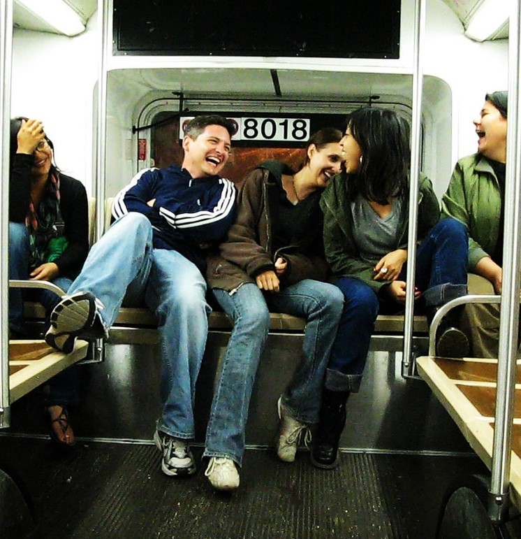 Friends laughing and chatting as they sit on a bench on public transportation.